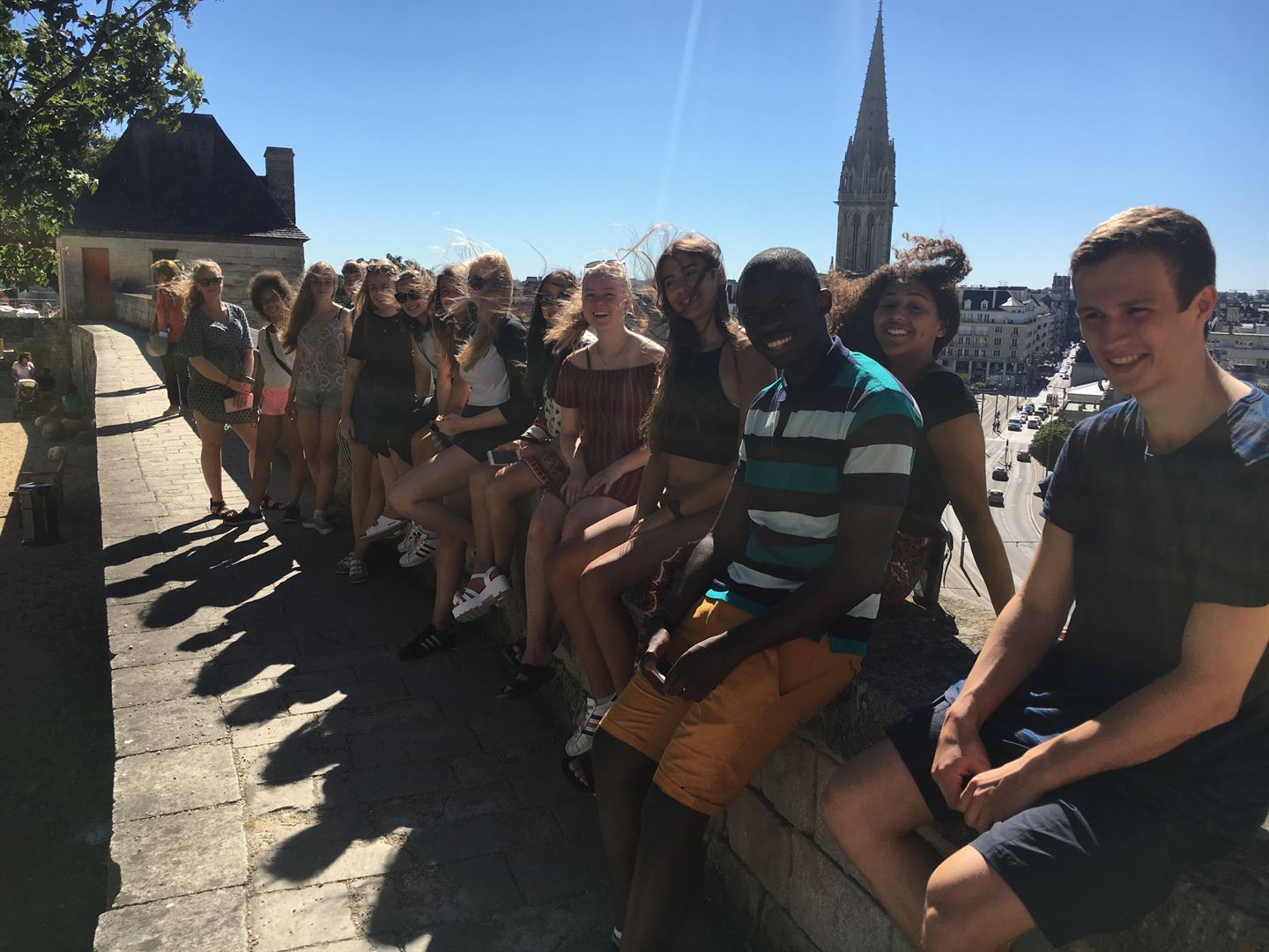 Ungdommer sitt på ved eit rekkverke med historiske bygg i bakgrunna.