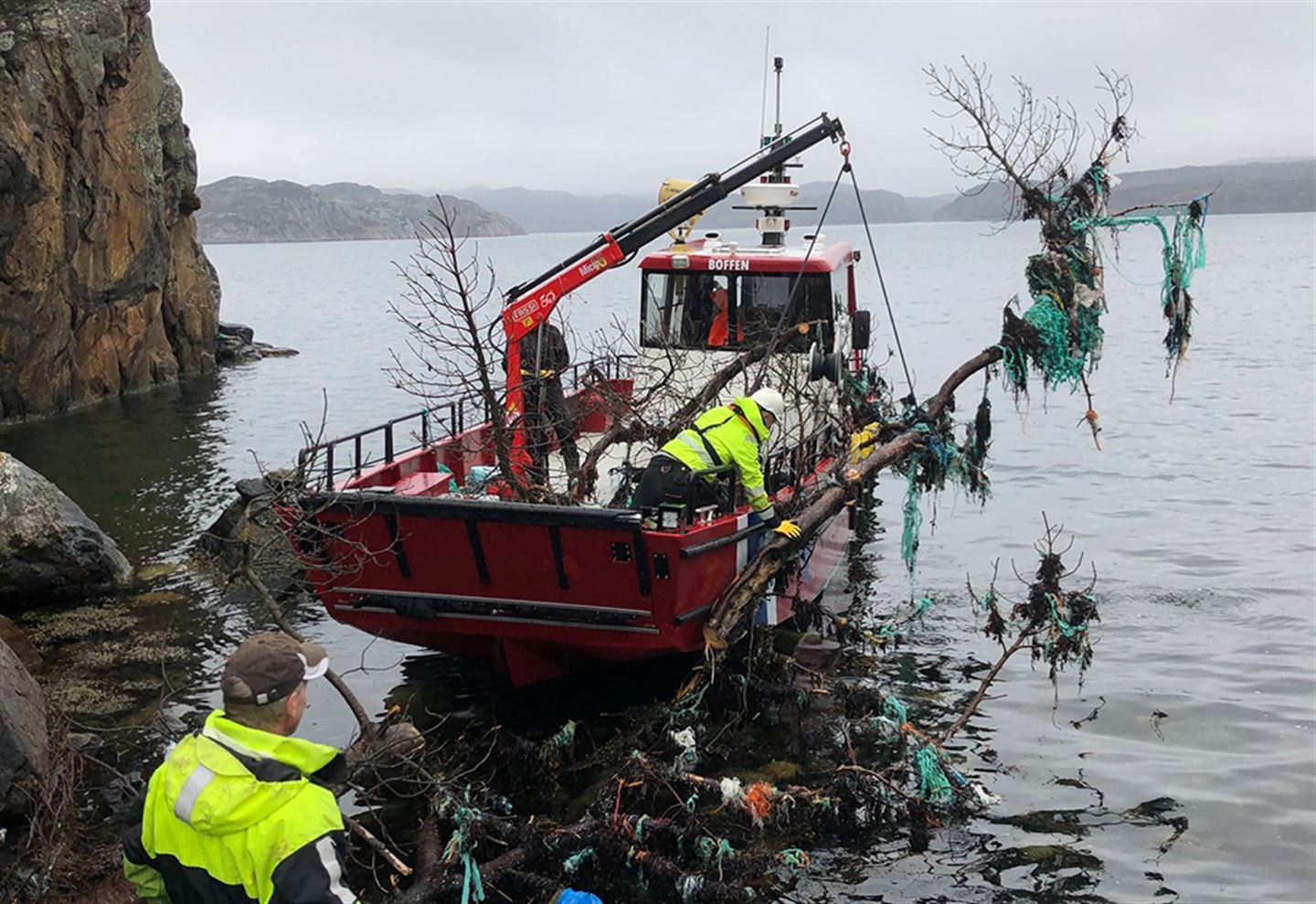 Foto av plastrydding i fjøra, med båt som hjelper til ute på sjøen.