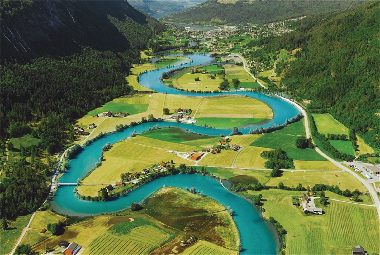 dronefoto som syner Stryneelva som buktar seg nedover dalen. Elva er blågrøn, medan markene og skogen rundt er grøn.