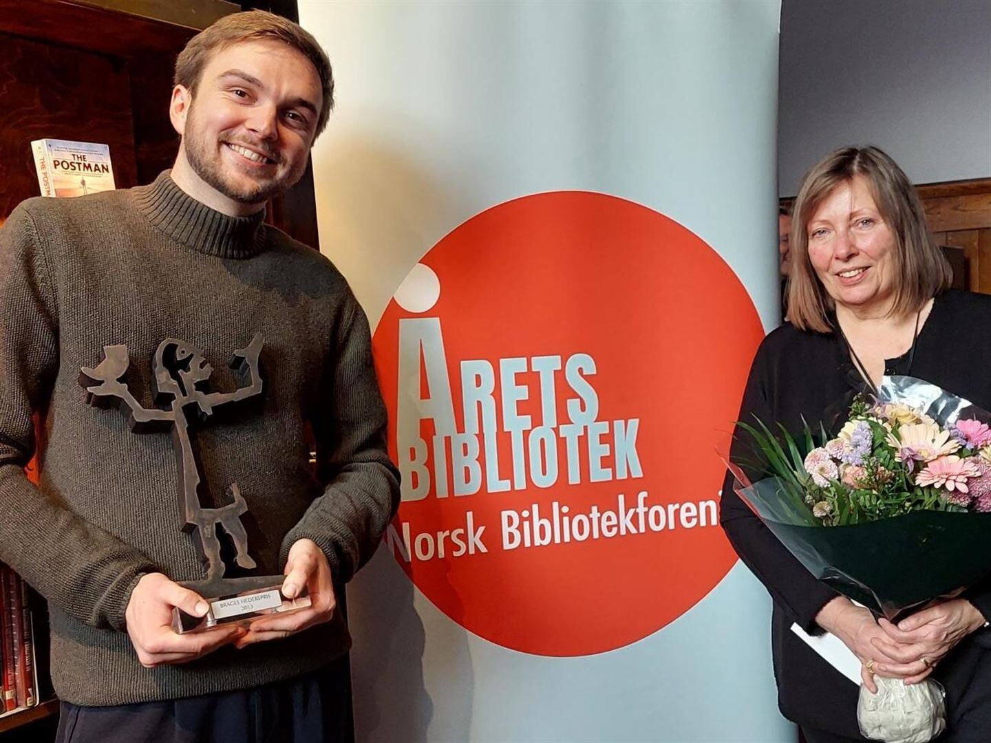 Mann og kvinne med blomster og statuett og plakat med teksten Årets bibliotek mellom seg.