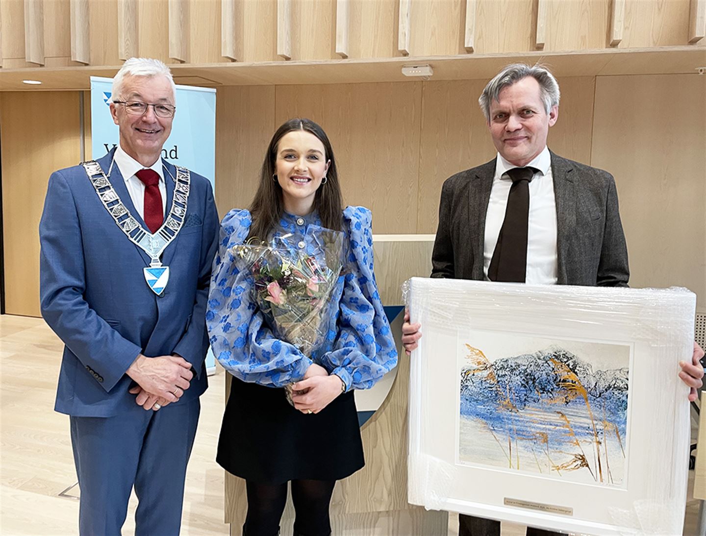 Tre personar stilte opp med blomster og kunstverk i hendene.