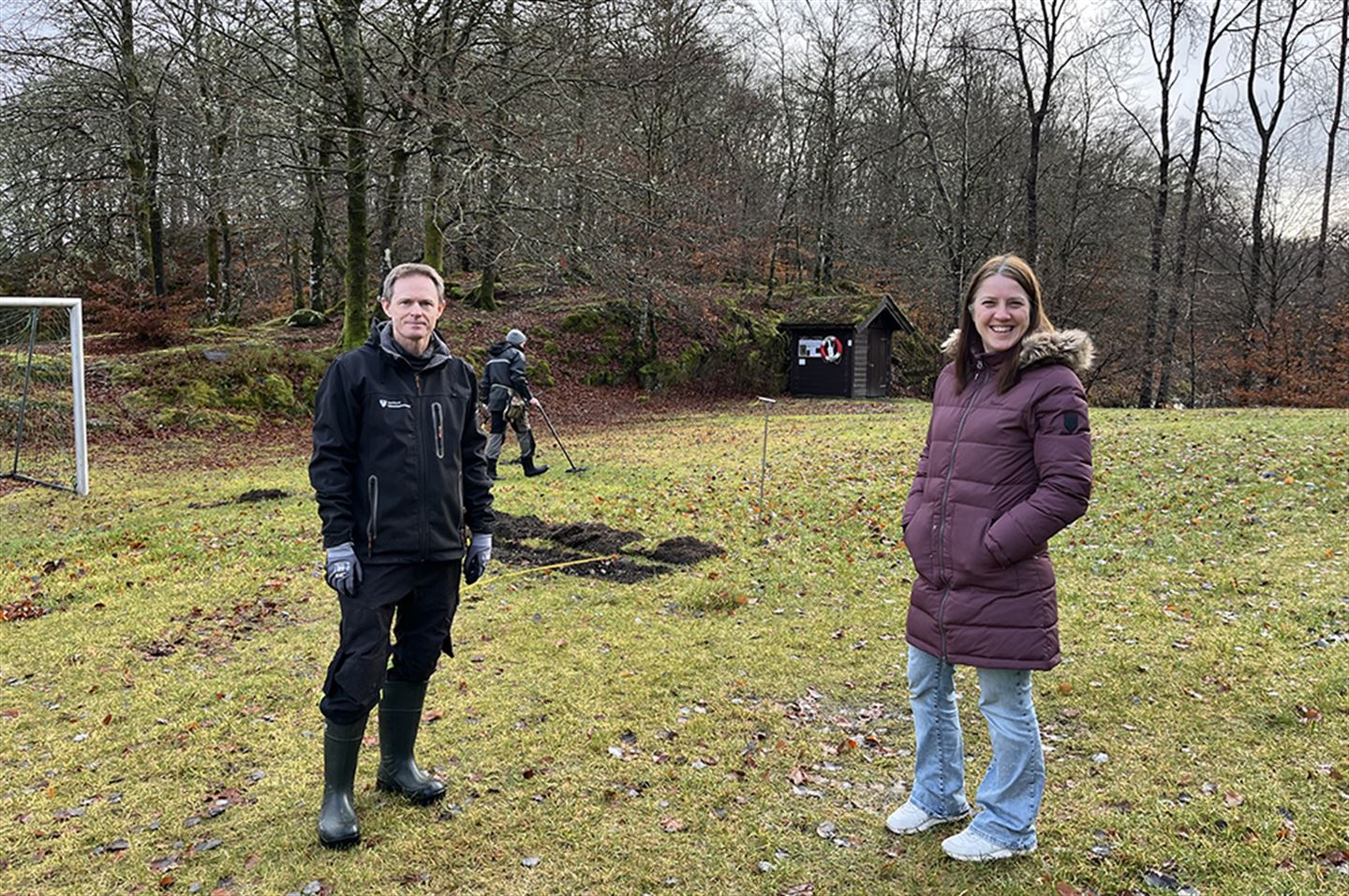 Mann og kvinne i område der det blir gjort arkeologiske registreringar i bakgrunnen.