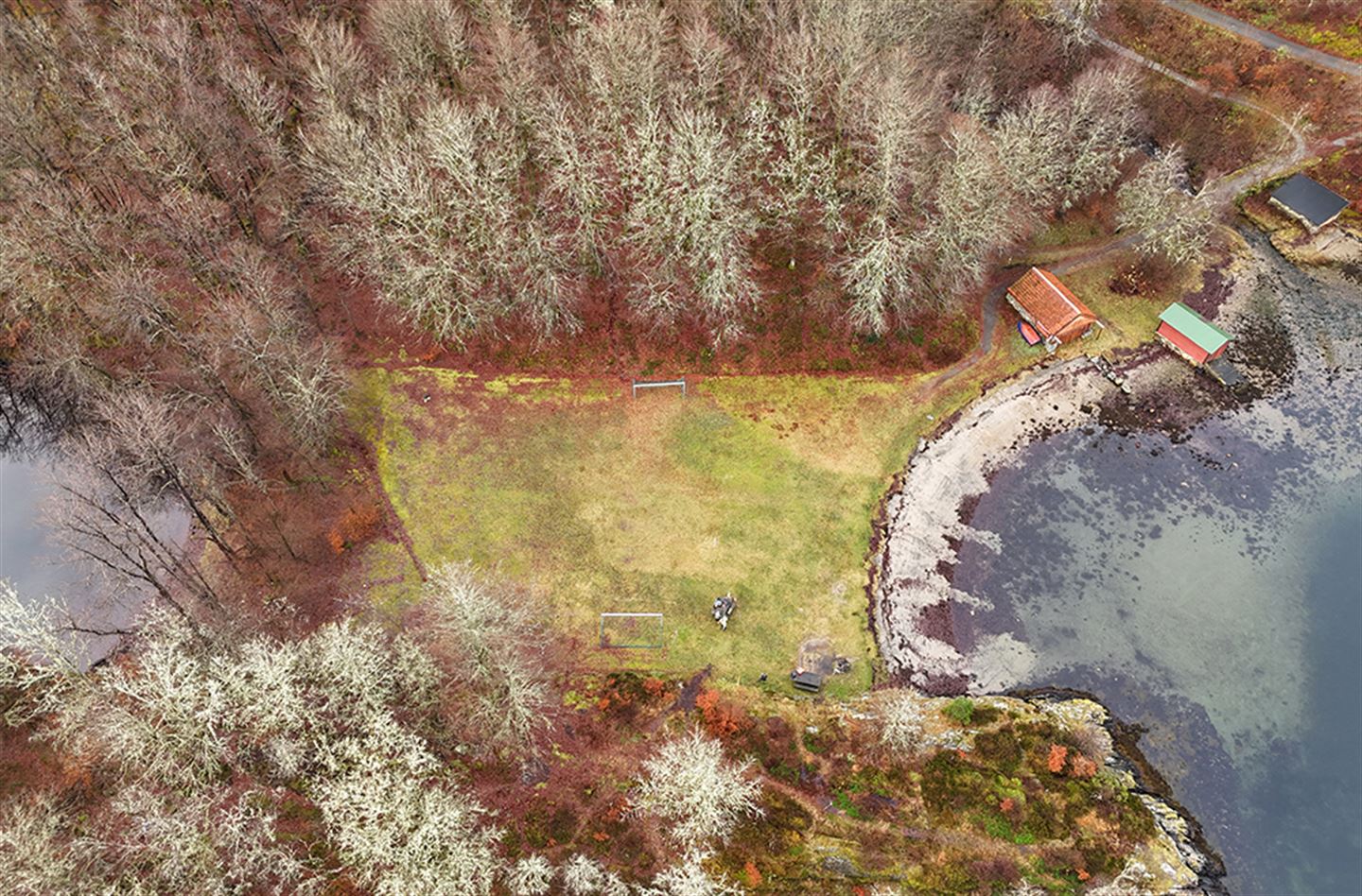 Dronefoto som syner flat grasmark, skog og fjord.