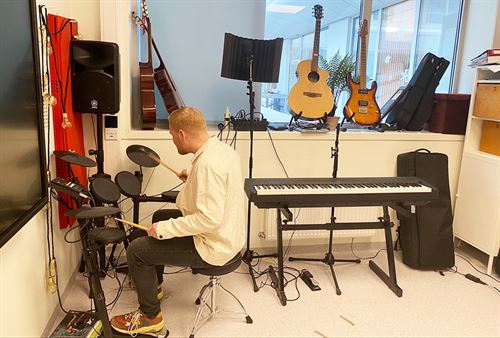 Ung mann som sit ved trommesett, med mange andre instrument rundt seg.