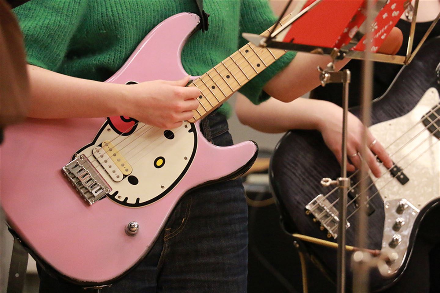 Nærbilde av to gitarar, ein rosa Hello Kitty-gitar og ein svart og kvit, saman med barnehender. 