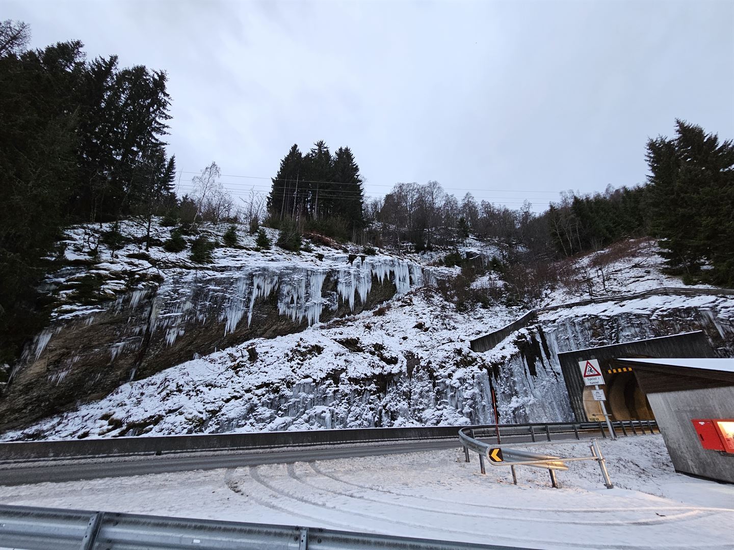store istappar heng over tunellinngangen og vegen inn mot tunellen, vinter, grå himmel, berg med istappar før og over tunellinngangen, Røneidstunellen. 