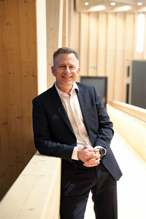 Ein mann i mørk dress og kvit skjorte lener seg på eit gelender. 