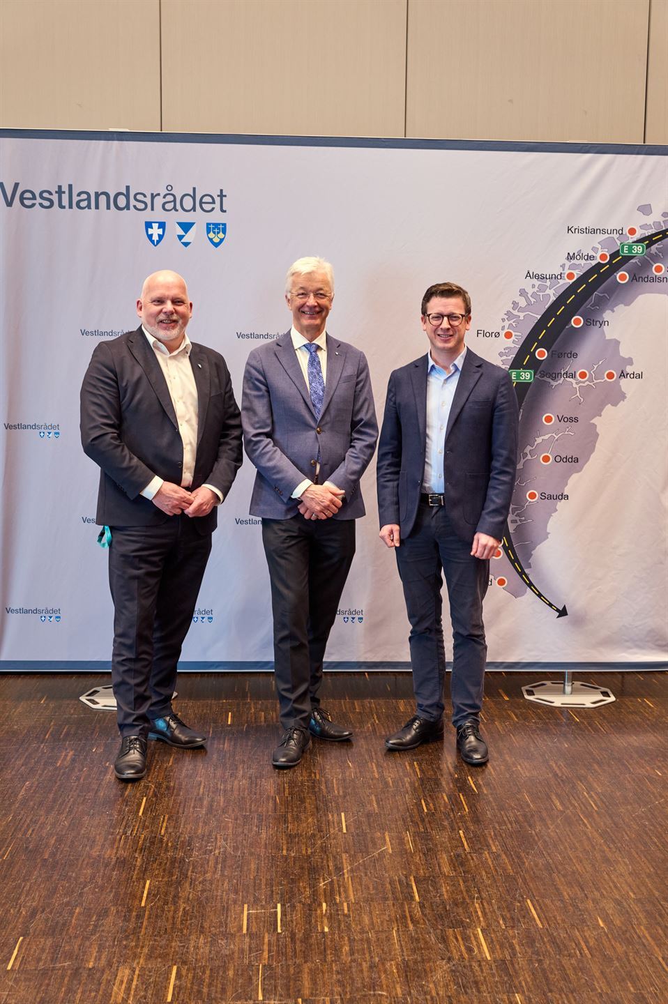 foto av tre personar foran ein banner