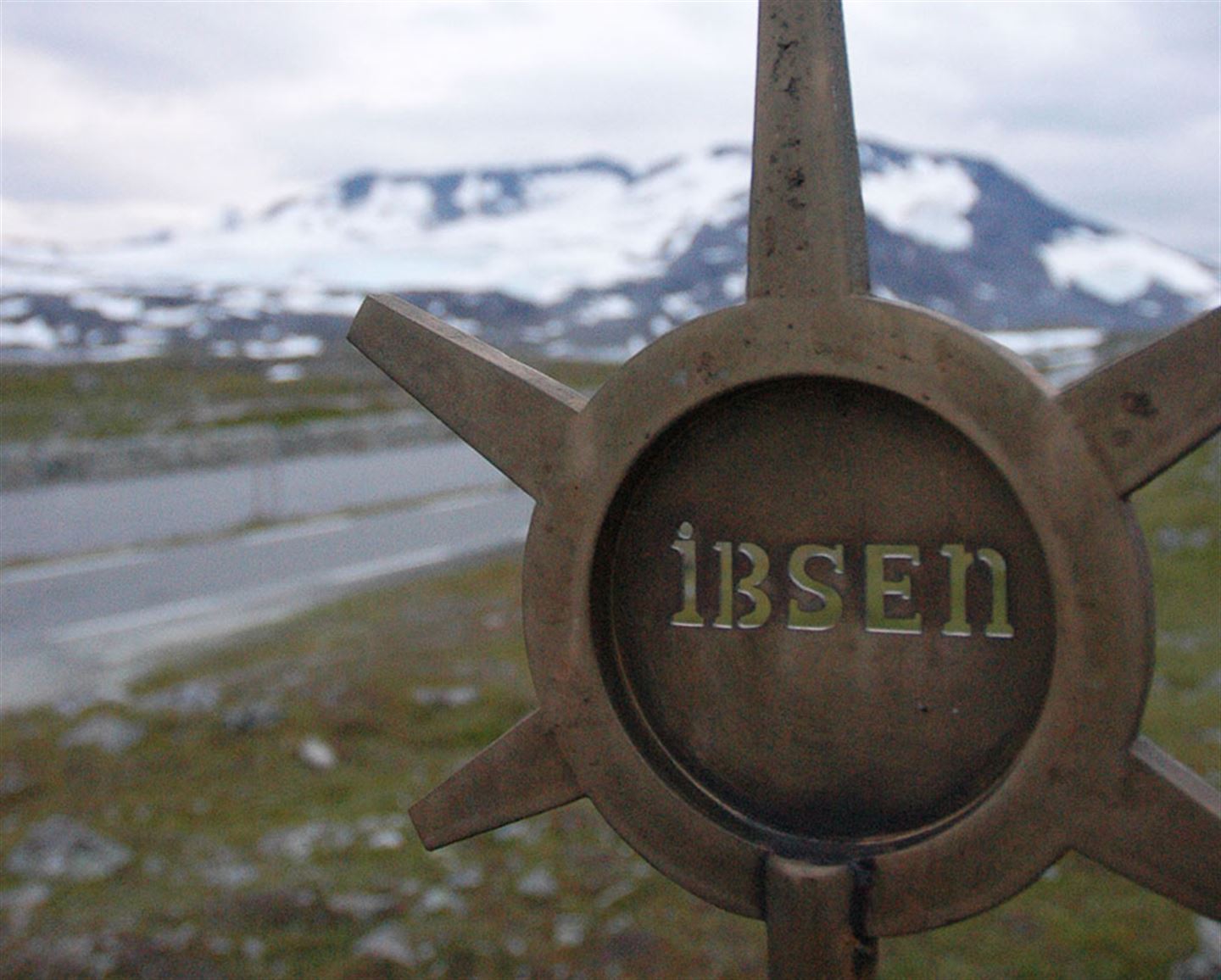 Lite monument på Sognefjellet, sirkel med strålar ut. Det står Ibsen i midten.