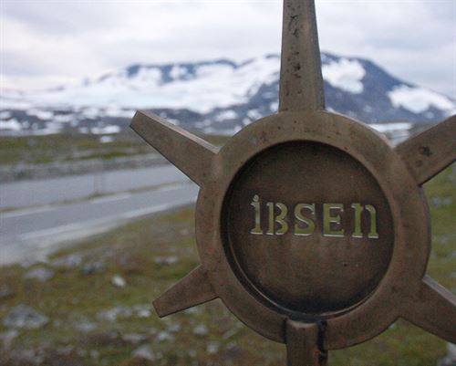 Lite monument på Sognefjellet, sirkel med strålar ut. Det står Ibsen i midten.