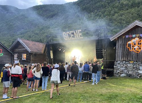Konsert på gamalt gardstun med gamle trebygg rundt scene med band og publikum framfor.