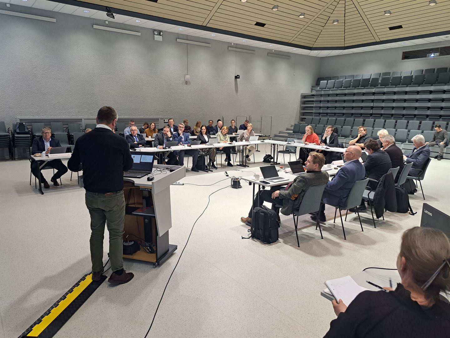 Eit møtelokale med menneske som sit rundt bord. 