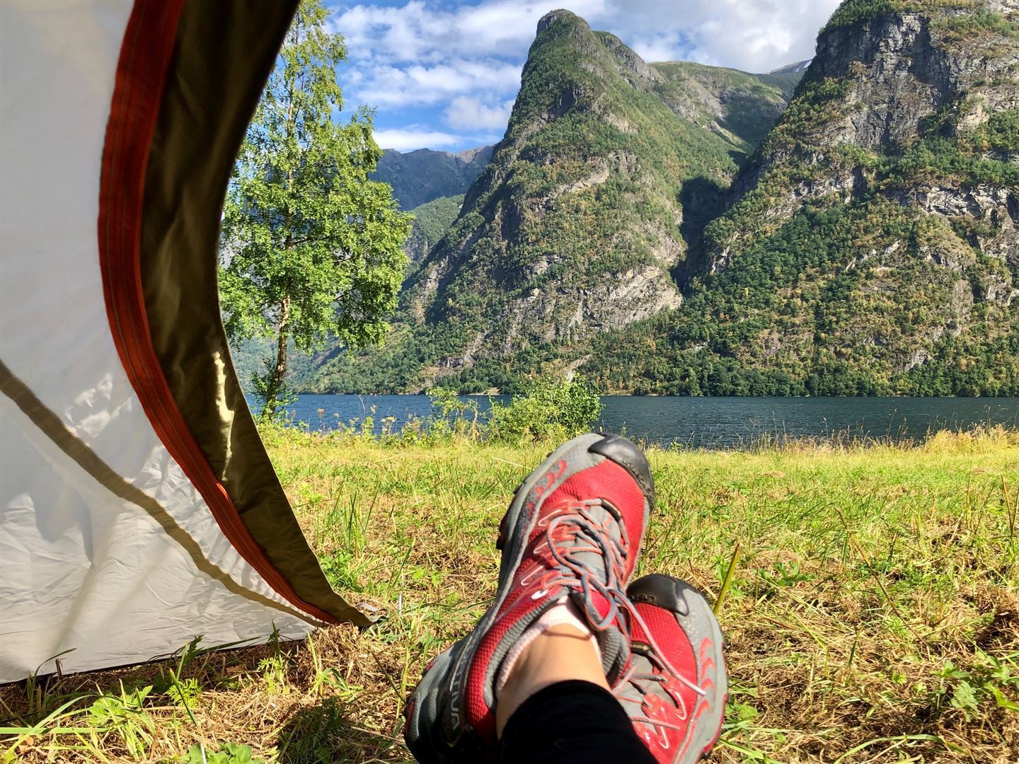 foto av eit par bein med tursko og teltduk og fjell i bakgrunnen