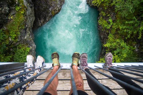Utsikt frå bru og rett ned i foss med fire par føter med joggesko i framgrunnen.