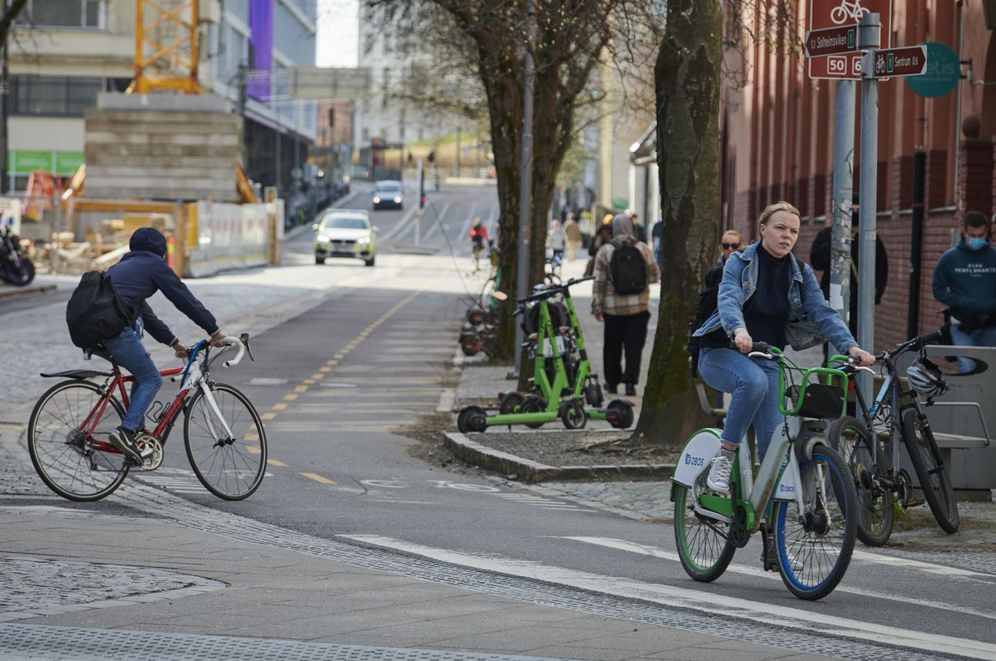 Trafikk i bygate i Bergen, to syklistar i gang og sykkelveg attmed fylkesveg. Elsparkesyklar står på fortauet. 