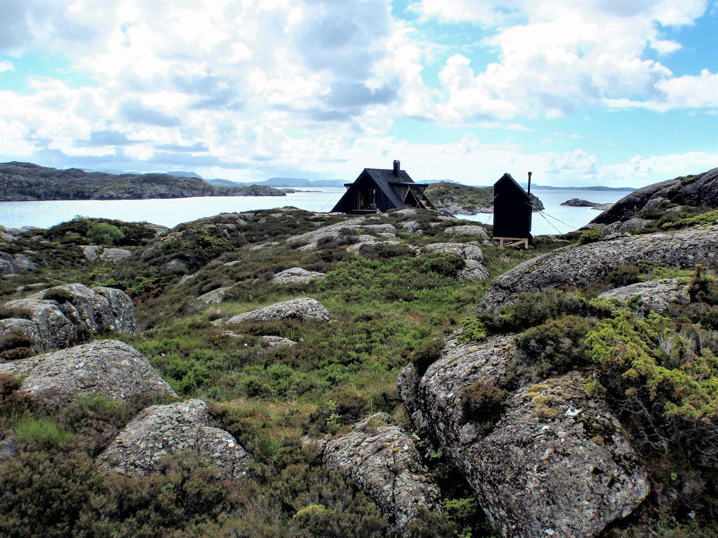 Bilde av ei dagsturhytte. Hytta står på svaberg nesten heilt ute i havgapet. Det er også ei mindre hytte ved siden av.