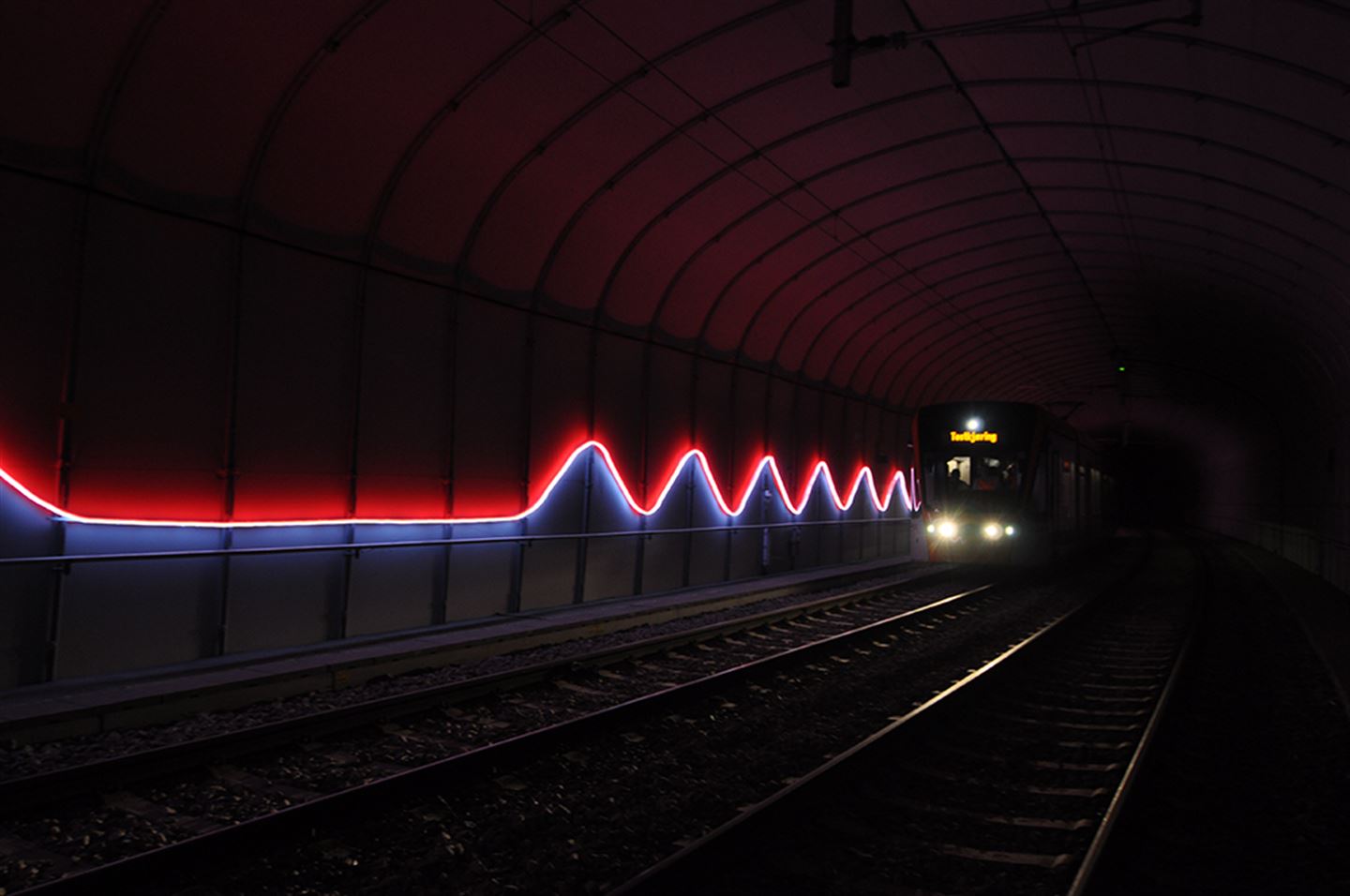 Foto av kunstverket Puls langs bybanetraseen. Det er raudt og blått lys inni ein bybanetunnel.
