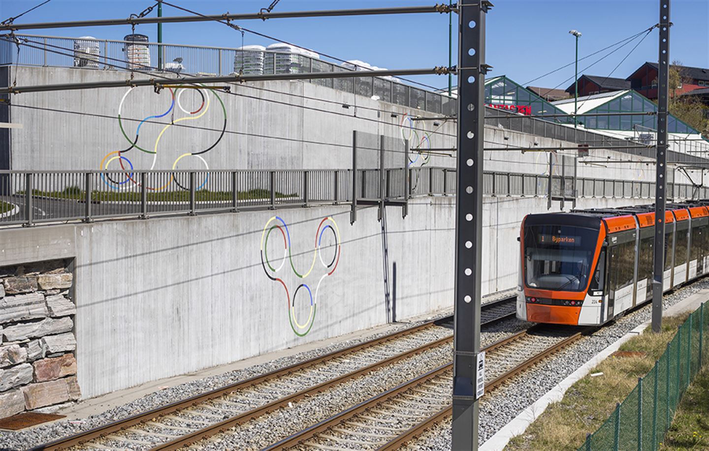 Foto av bybanen. På betongveggen ved bana syner kunstverket Sirkelspill, som er fargerike figurar målt på betong.