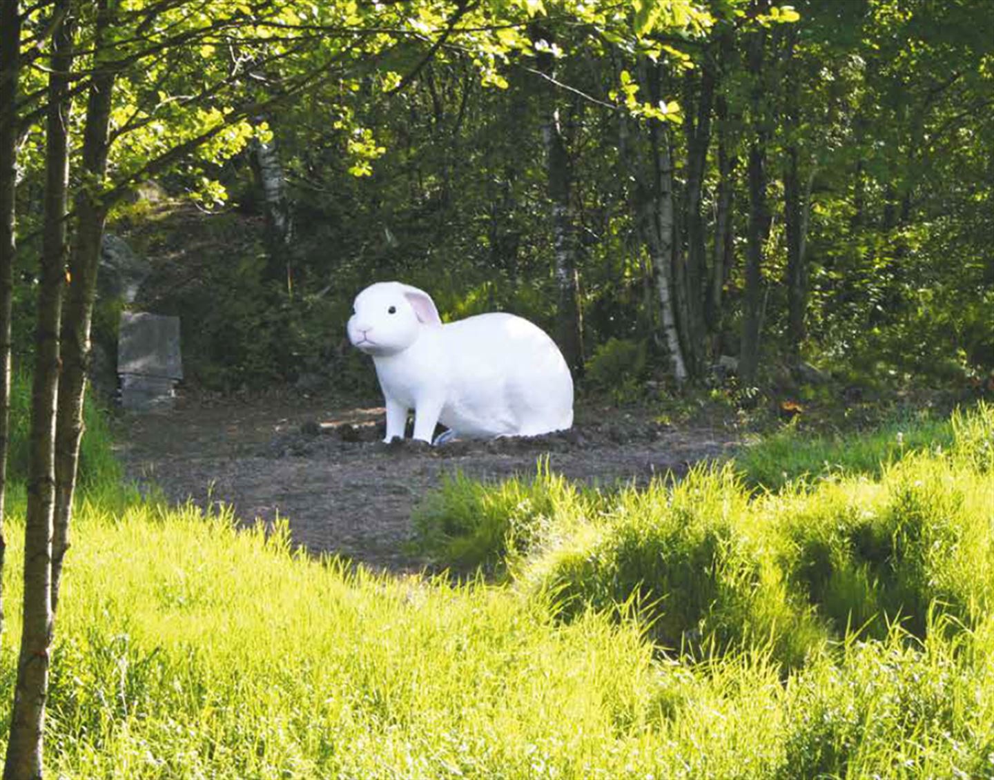 Foto av kunstverket The White Rabbit langs bybanetraseen. Det er ei stor kvit kanin som står i skogen.
