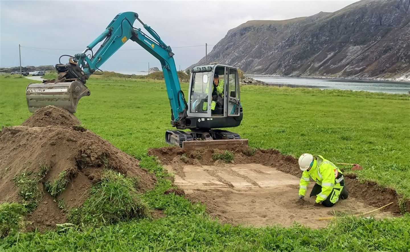Arkeolog og gravemaskin i arbeid i sjakt på Grotlesanden.
