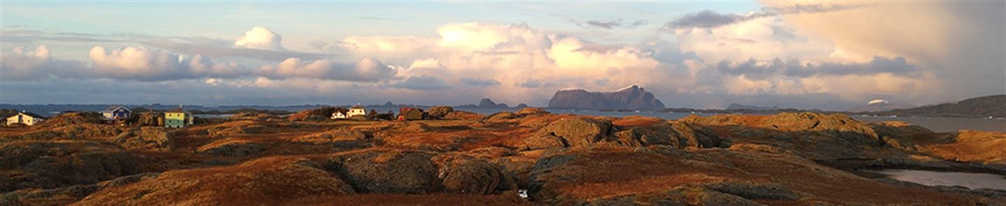 Foto som viser øya Gåsvær i solskinn med fjellkjede i bakgrunnen