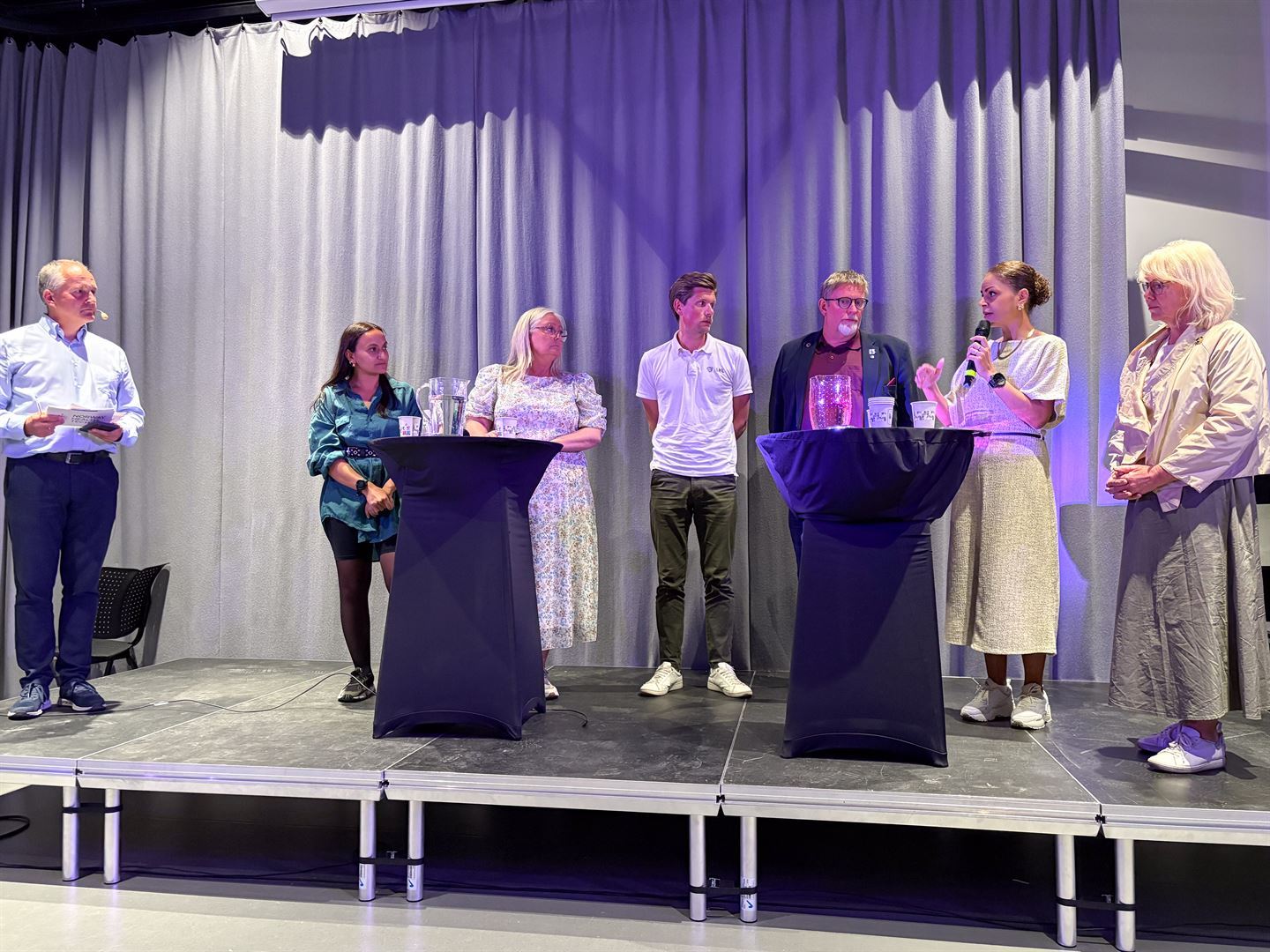Sju personer står på en scene