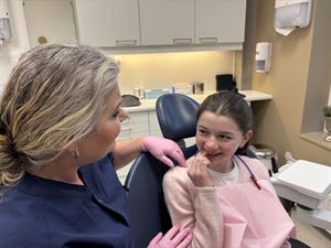 Jente på tannklinikk, saman med tannpleiar, som peiker på tanna si