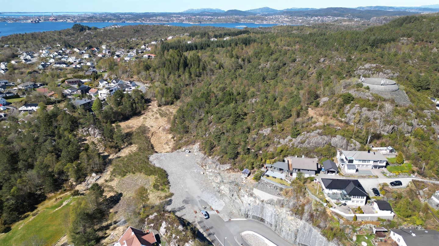 Bilete som viser hus, skog og gruslagt felt eit stykke inn i terrenget.