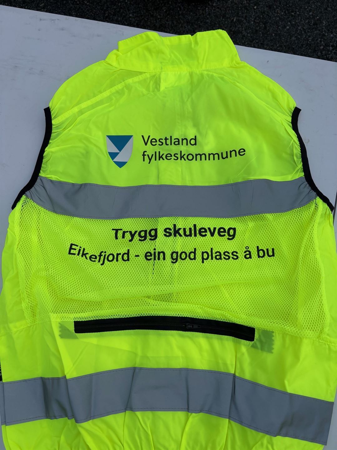 Gul refleksvest ligg på eit bord. Teksten på ryggen av vesten seier Trygg skuleveg og Eikefjord - ein god plass å bu.