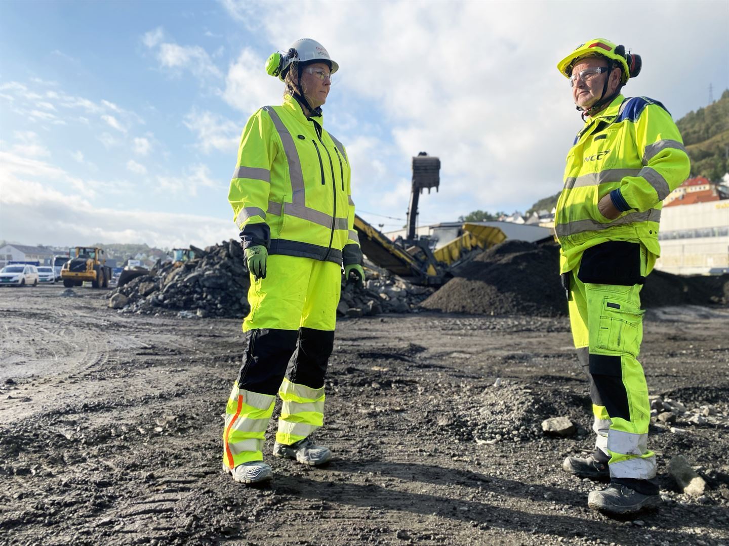 to personer i gult arbeidsutstyr og hjelper på byggeplass. 