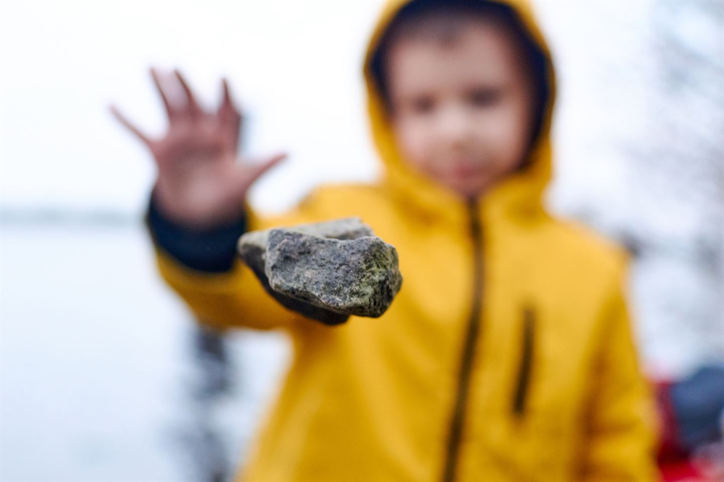 gutt med gul regnfrakk kaster liten stein i lufta