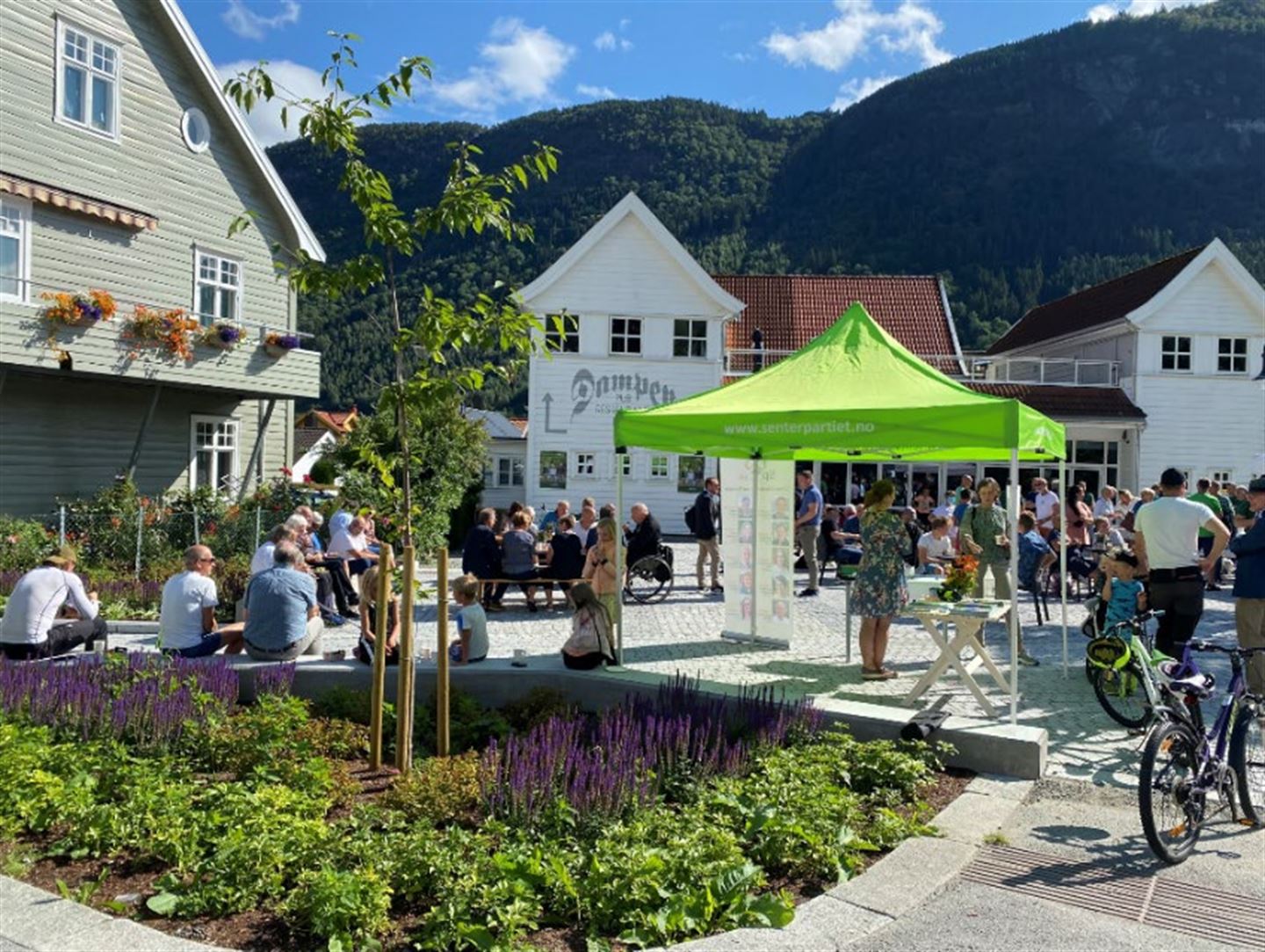 Bilete viser torget i bruk på sensommeren 2021 i samband med valkampen. Det er stand frå Senterpartiet, og mange menneske har samla seg på torget.