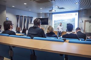 Foto av auditorium kor ein person presenterer for ei gruppe tilhøyrar