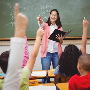 lærer i klasserom peker ut over elevene som rekker opp handa. 